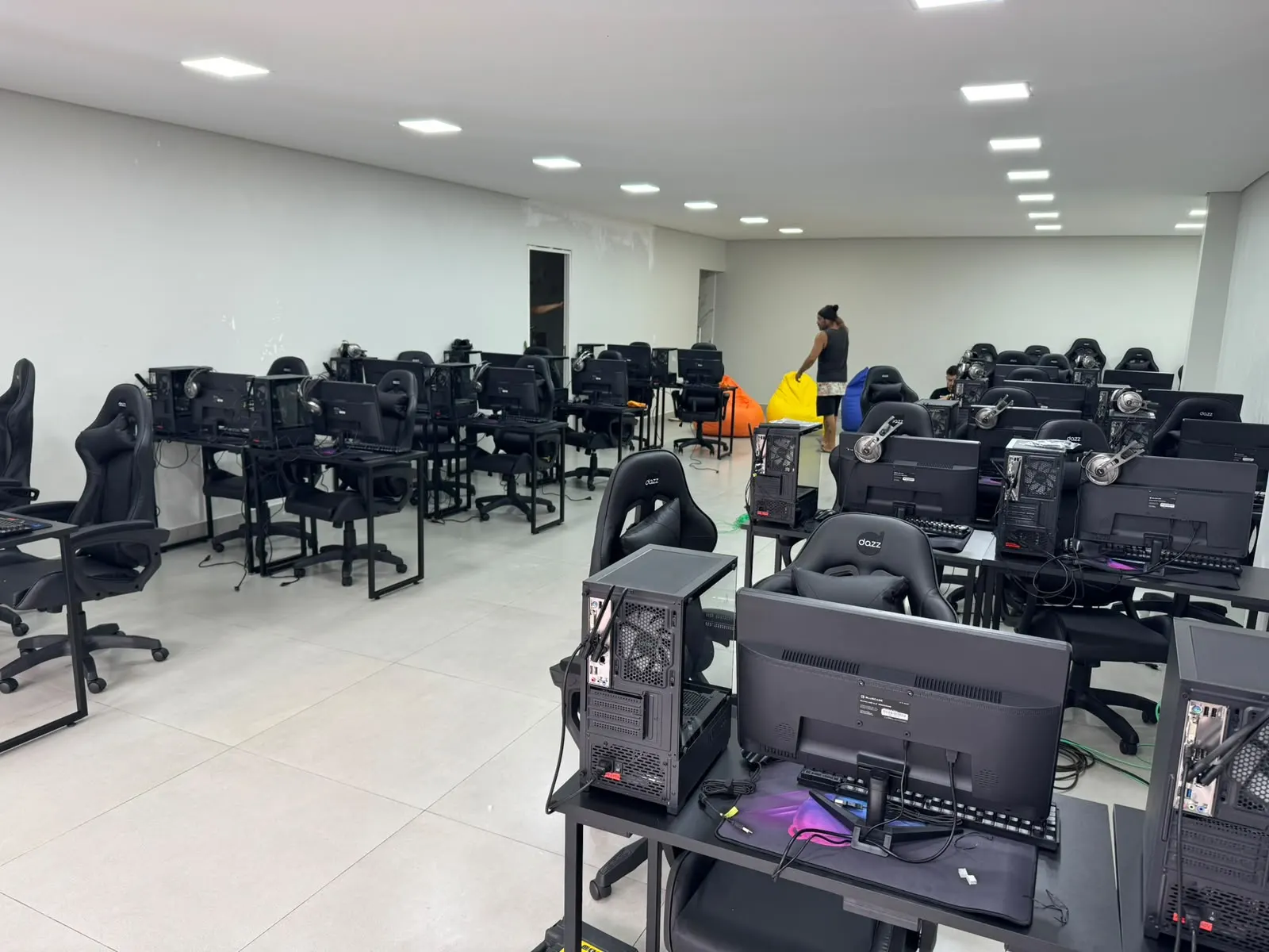 Sala com dezenas de computadores, monitores e cadeiras montados para capacitação